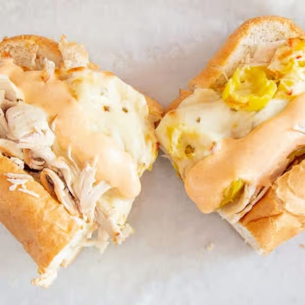 Two halves of a Monti's chicken cheesesteak sandwich, topped with melted cheese and sauce.