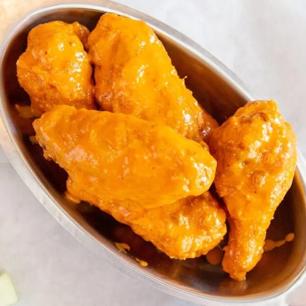 Monti's American-style chicken wings, coated in a vibrant orange sauce, served in a silver bowl.