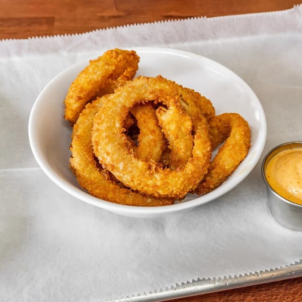 A white bowl filled with golden-brown onion rings, served with a side of dipping sauce.