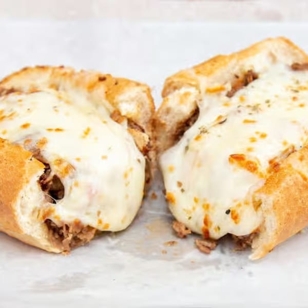 Two halves of a Monti's cheesesteak sandwich, filled with meat and melted white cheese.