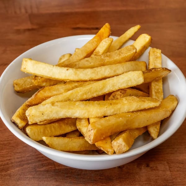 A white bowl filled with golden-brown, seasoned Monti's American-style french fries on a wooden table.