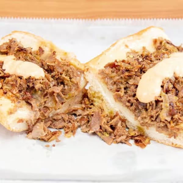 Monti's cheesesteak, sliced in half, revealing steak, onions, and cheese sauce on a white surface.