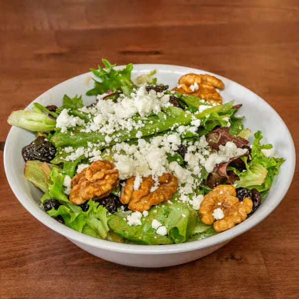 A fresh Monti's salad with mixed greens, crumbled feta, walnuts, and dried cranberries in a white bowl.
