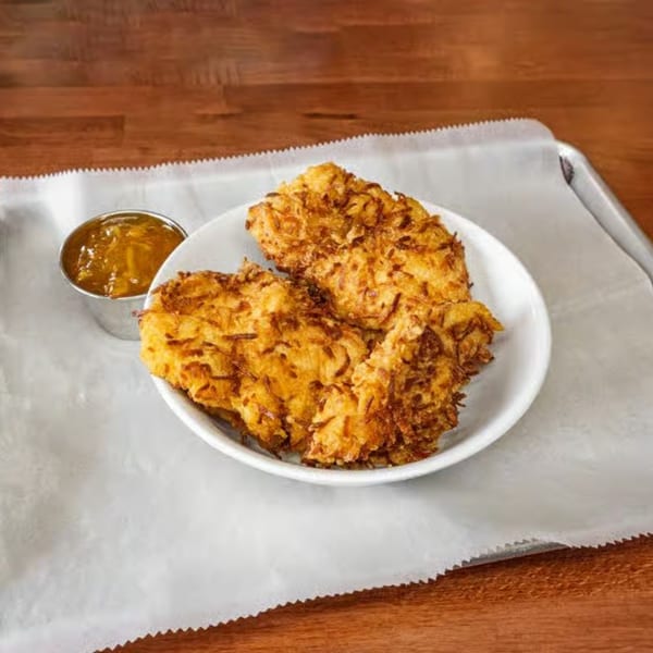 Crispy golden-brown hash brown patties on a white plate with a side of orange marmalade.